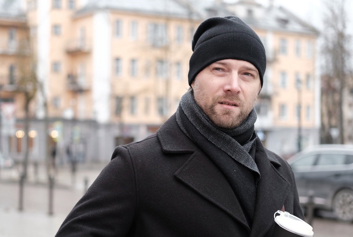 mężczyzna w wieku 30 plus w czarnej czapce i płaszczu stoi na ulicy z kubkiem w ręku