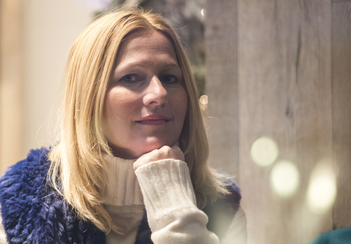 kobieta w wieku około 40 lat blondynka w niebieskiej kamizelce ze sztucznego futerka siedzi zamyślona