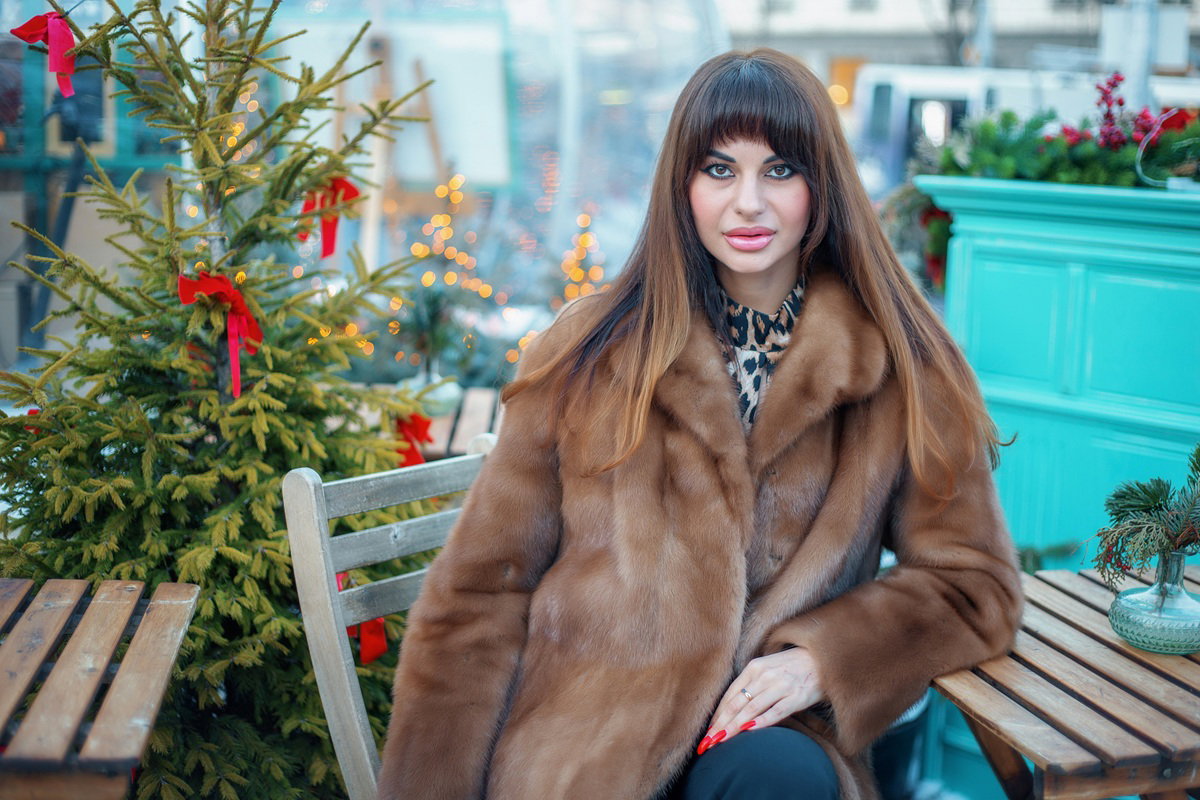 kobieta w wieku 30 plus długie włosy z grzywką i w futrze siedzi w kawiarni koło choinki