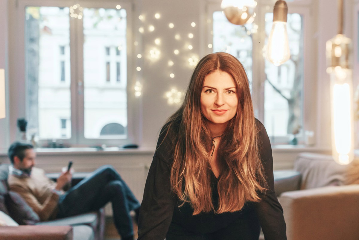 kobieta w wieku 30 plus stoi w salonie w tle mężczyzna a ona lekko się uśmiecha