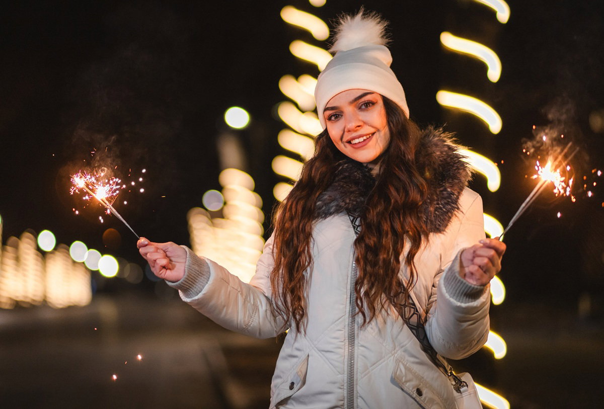 kobieta w wieku 25 plus w jasnej kurtce i czapce z pomponem trzyma sztuczne ognie