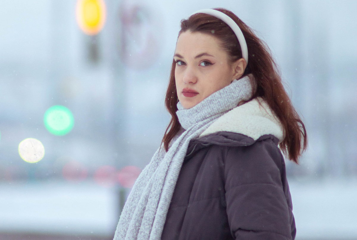 kobieta w wieku 25 plus stoi na ulicy w szali i z opaską na głowie zamyślona i smutna