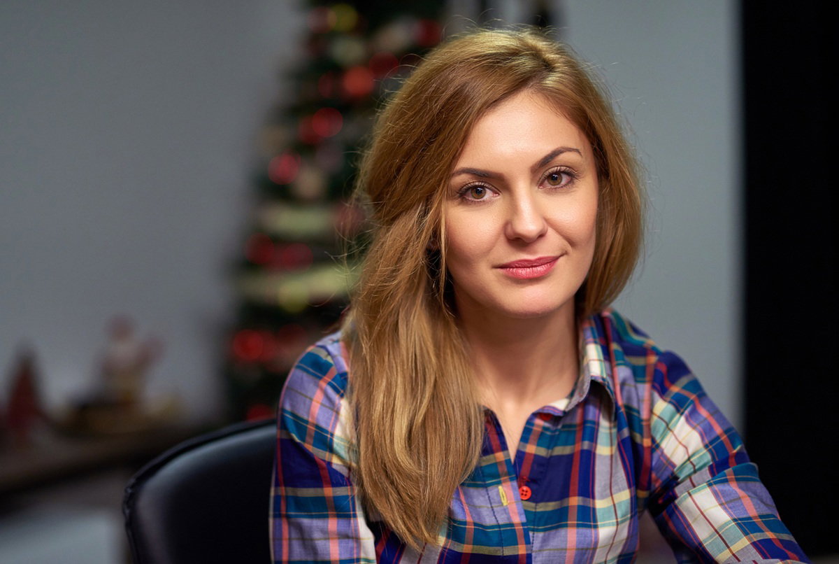 kobieta w wieku około 30 lat w kraciastej koszuli siedzi na tle choinki zamyślona