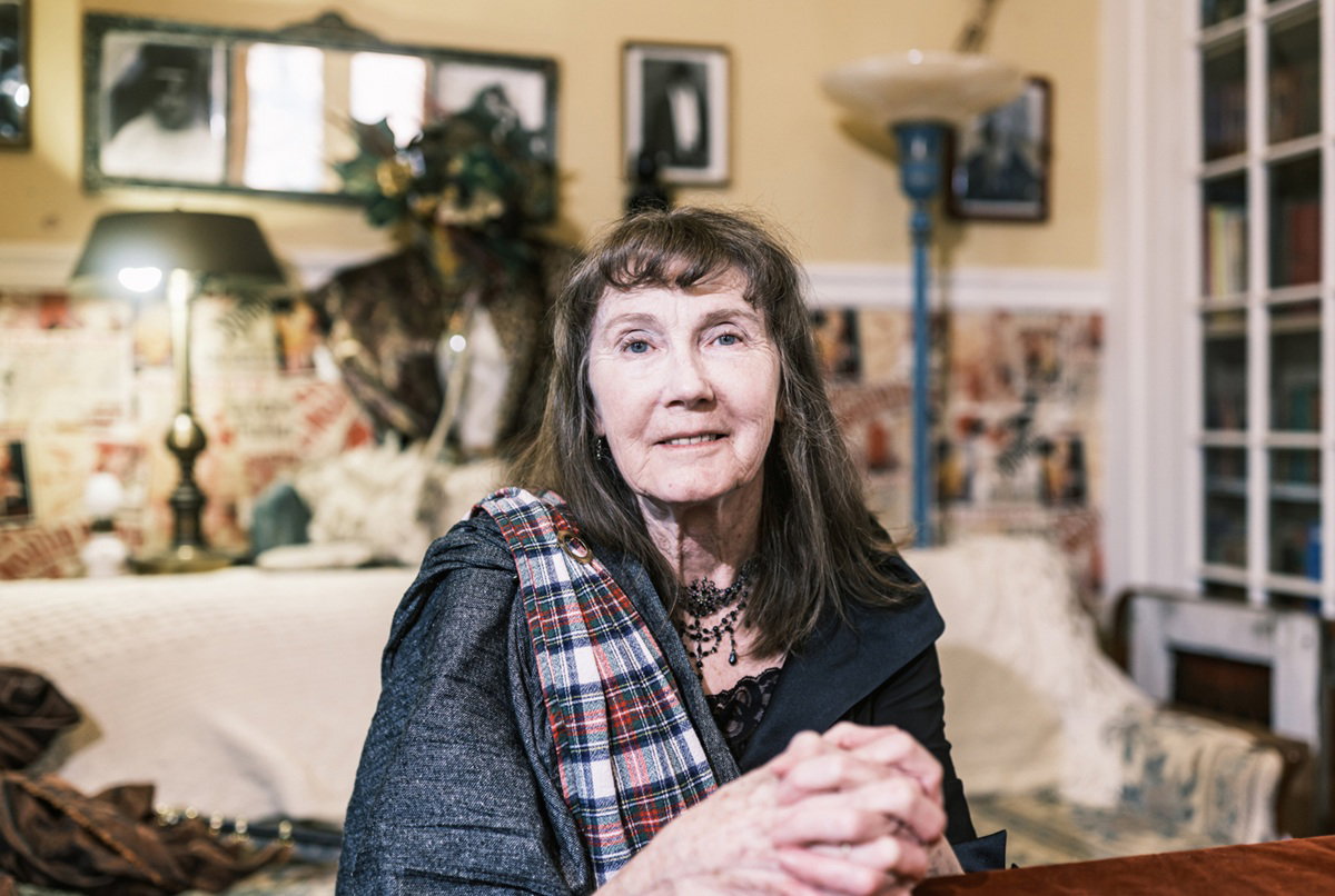 kobieta w wieku około 70 lat w naszyjniku i z długimi włosami z grzywka modli sie przy stole w swoim pokoju