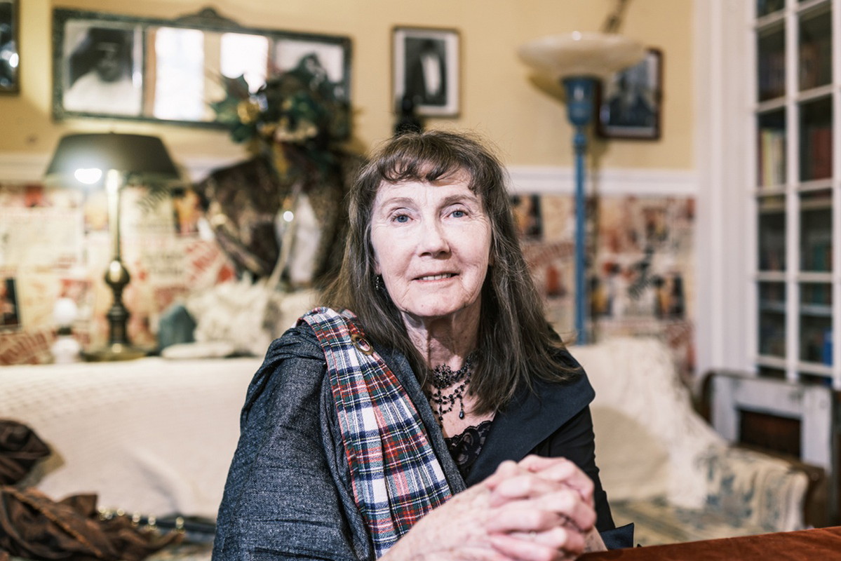 kobieta w wieku około 70 lat w naszyjniku i z długimi włosami z grzywka modli sie przy stole w swoim pokoju