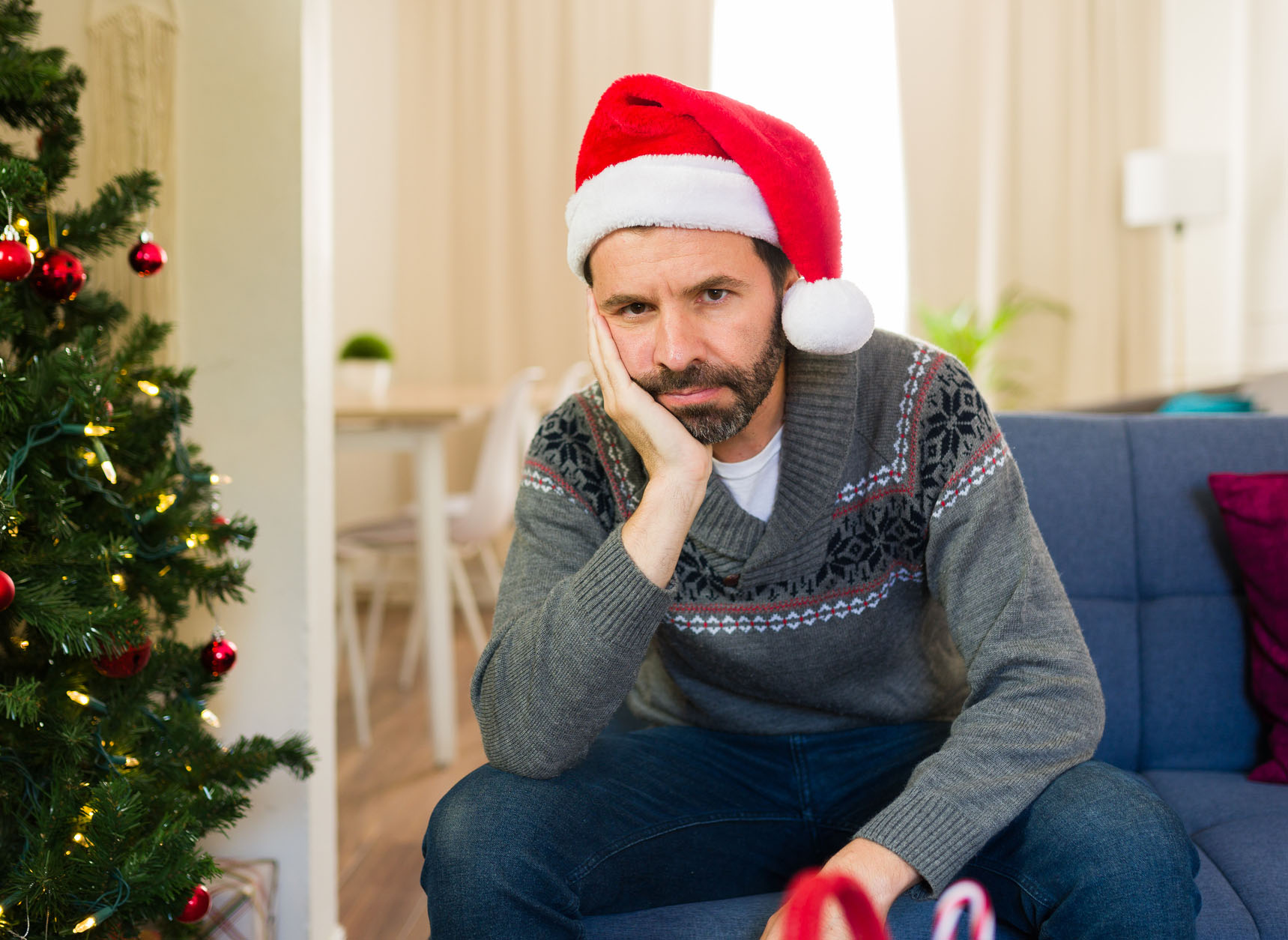 Lonely and depressed man in santa hat sitting on couch at home during christmas season