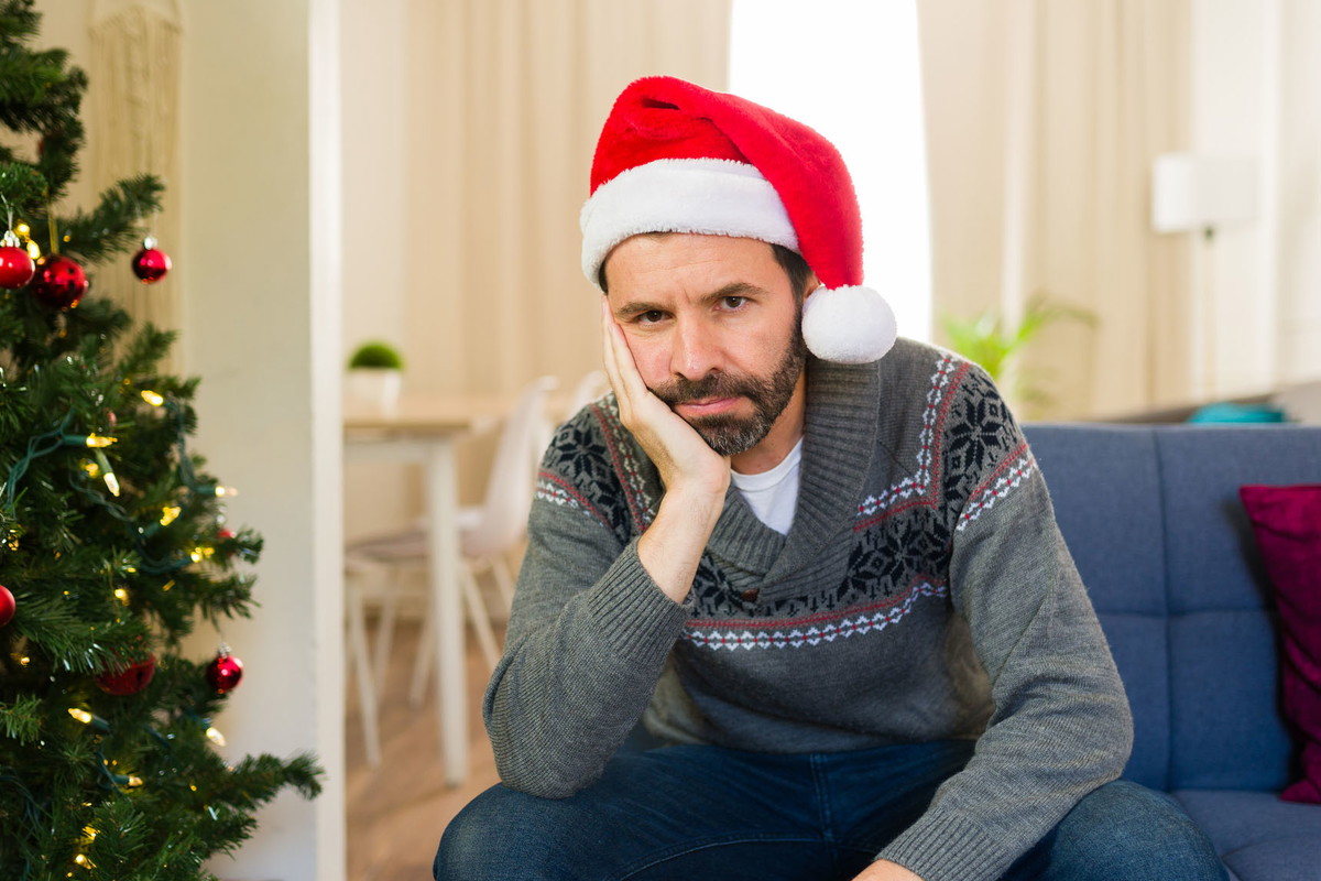 Lonely and depressed man in santa hat sitting on couch at home during christmas season