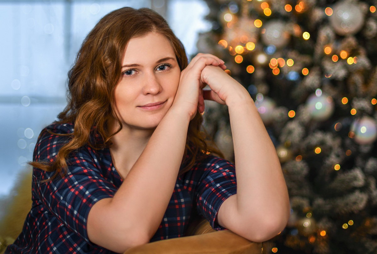 kobieta w wieku 30 plus siedzi na tle okna i choinki zamyślona