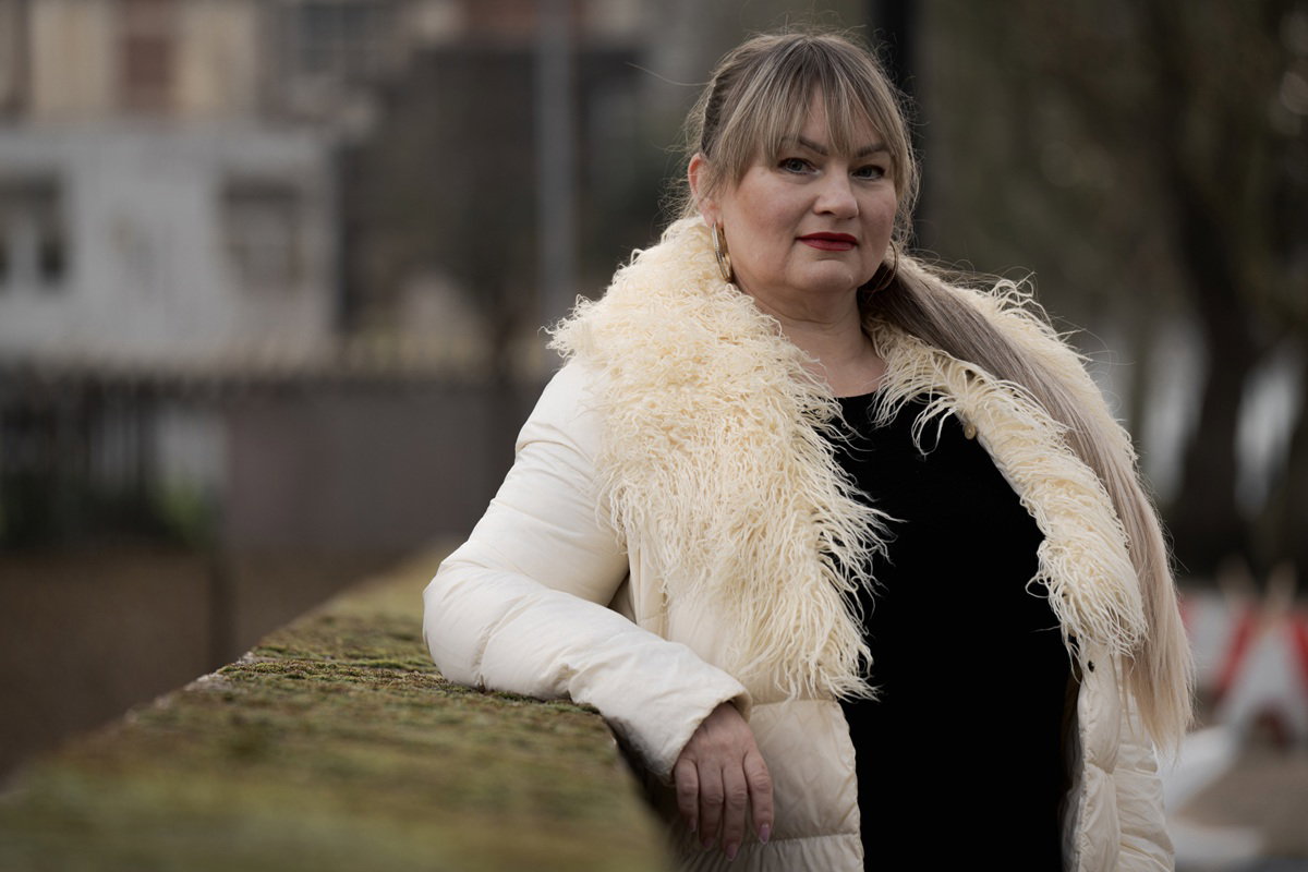 kobieta w wieku około 40 lat blondynka z kurtką z fantazyjnym kołnierzem stoi zadowolona przy moście