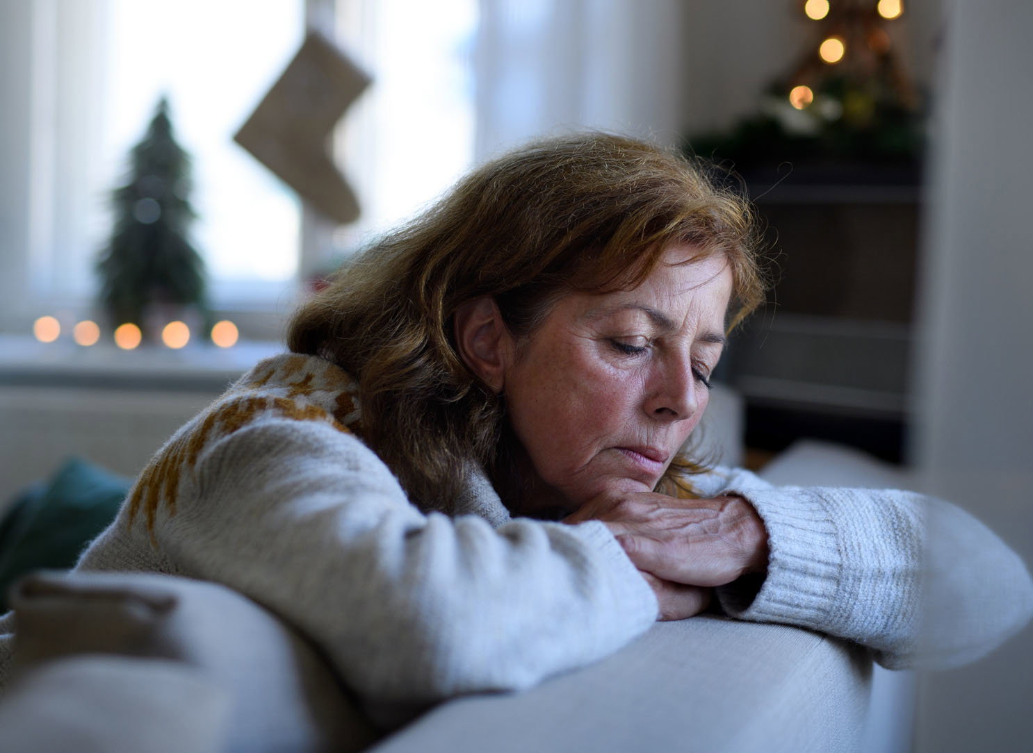 Lonely senior woman sitting and sleeping on sofa indoors at Christmas, solitude concept.