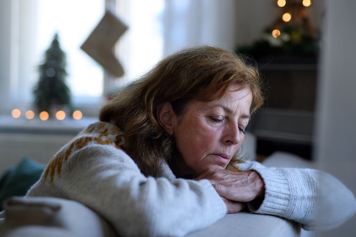 Lonely senior woman sitting and sleeping on sofa indoors at Christmas, solitude concept.