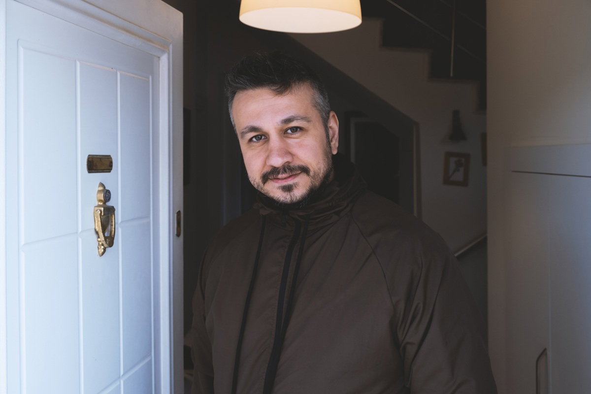 mężczyzna w wieku 40 plus stoi przy drzwiach w kurtce i lekko się uśmiecha