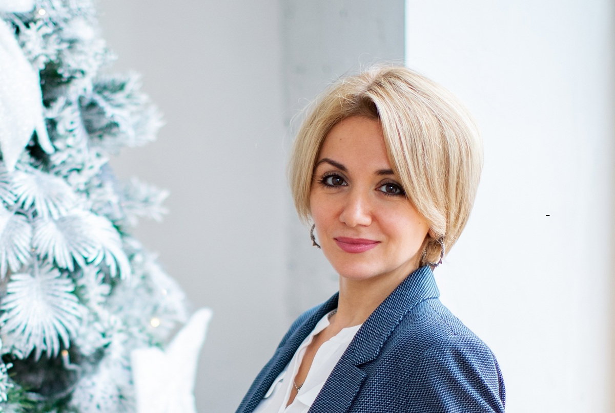 kobieta blondynka w wieku 30 plus stoi przy choince z miną lekko kpiącą