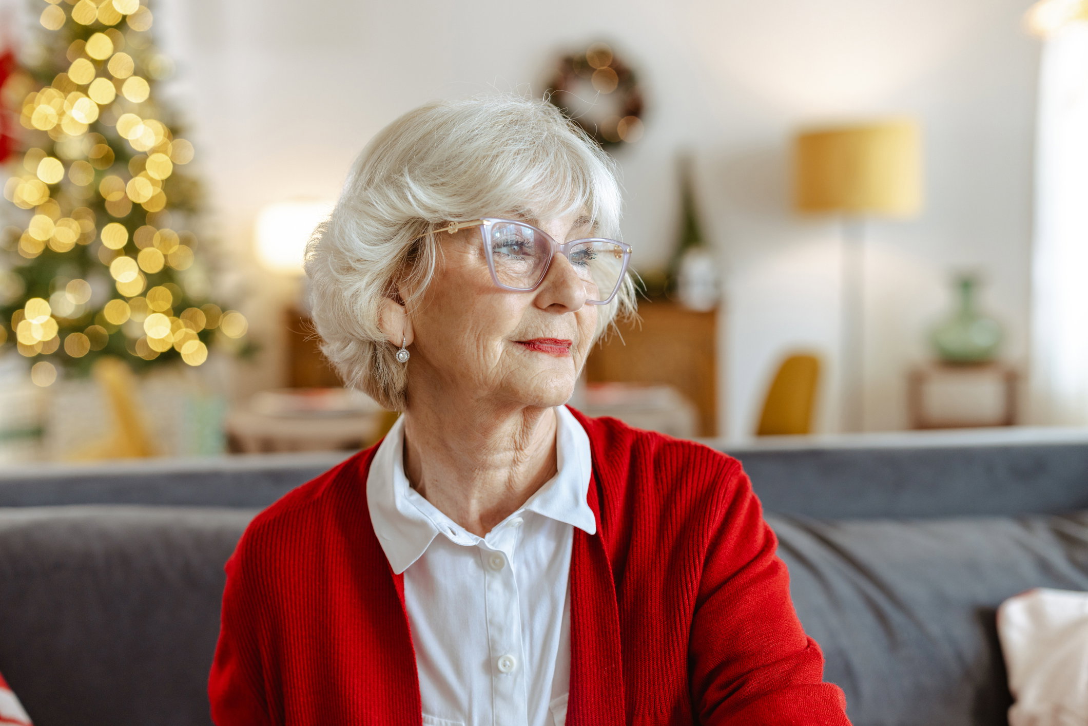 Elegant senior woman in a red cardigan sits on the sofa during Christmas at home