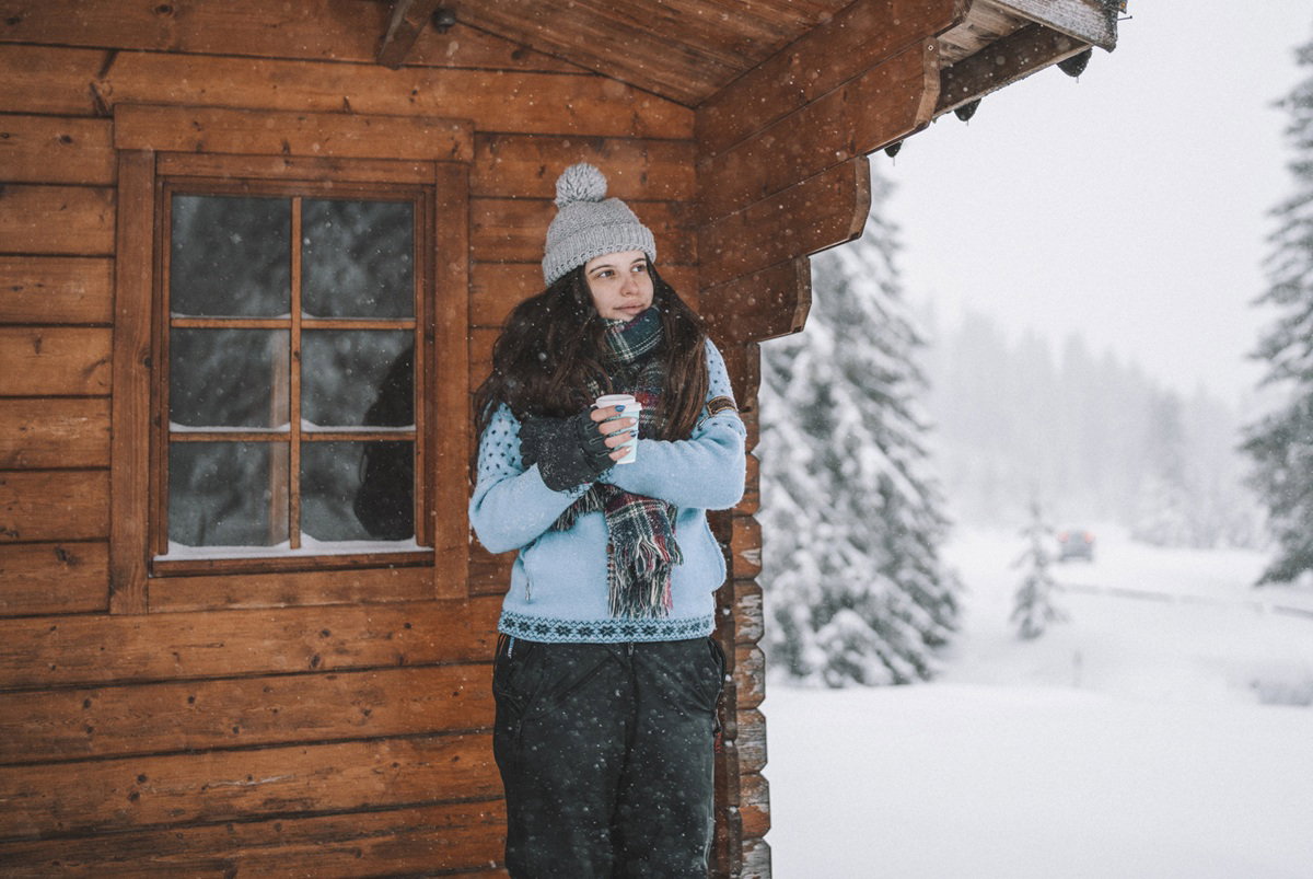 kobieta w wieku 25 plus stoi na ganku górskiego domku z kubkiem kawy w ręce