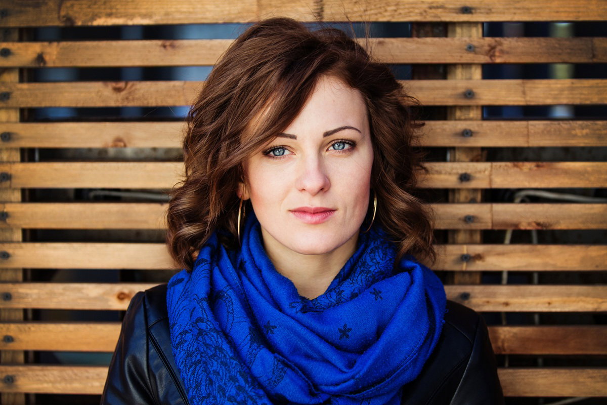 kobieta w wieku 30 plus w niebieskim szalu na szyi stoi na tle drewnianego przepierzenia na balkonie