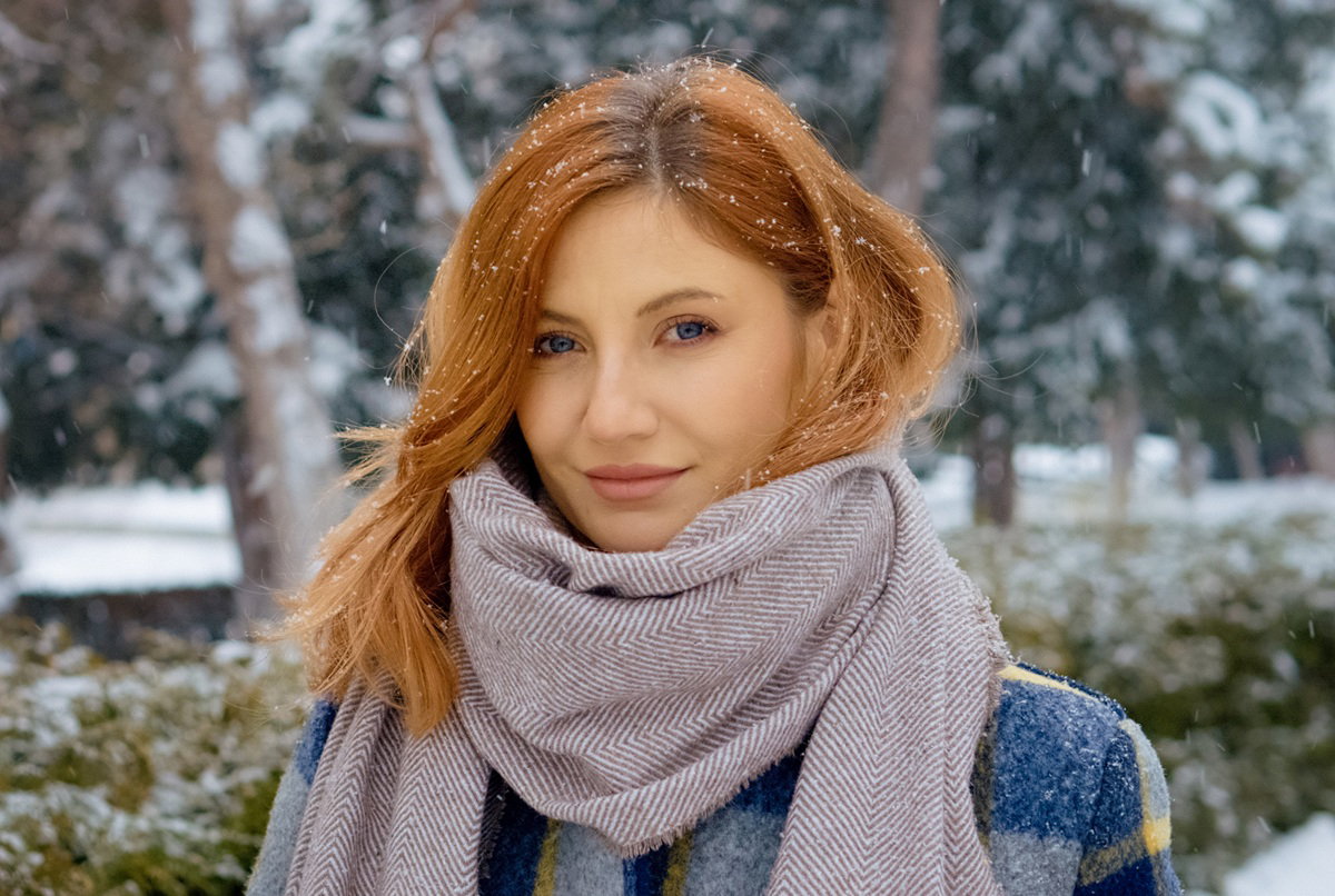 kobieta w wieku 30 plus w szalu stoi na zewnątrz w padającym śniegu