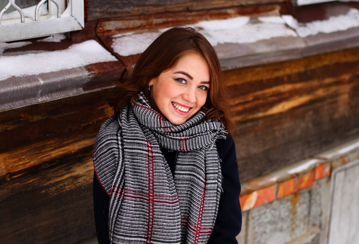 kobieta w wieku 30 plus stoi na tle ściany drewnianego domu i się uśmiecha