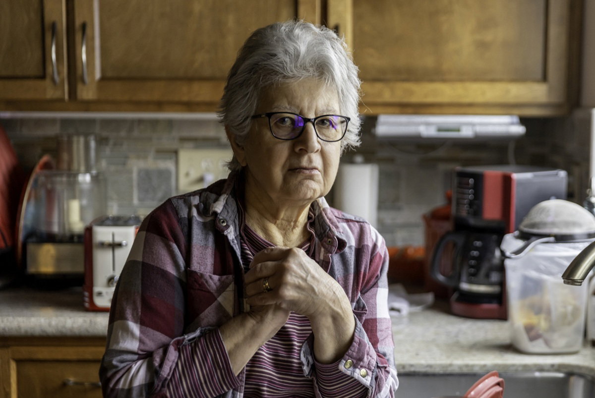 kobieta w wieku 70 plus w okularach stoi smutna w kuchni nad zlewem