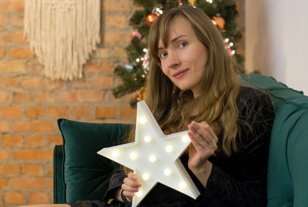 kobieta w wieku 35 plus z gwiazdka w rękach lekko zamyślona siedzi na kanapie na tle choinki