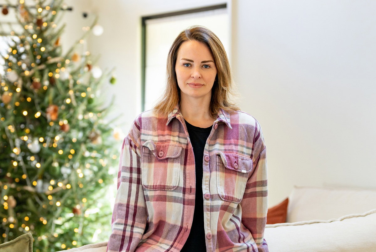 kobieta w wieku około 40 lat w koszuli w kratę opiera się o kanapę na tle choinki poważna