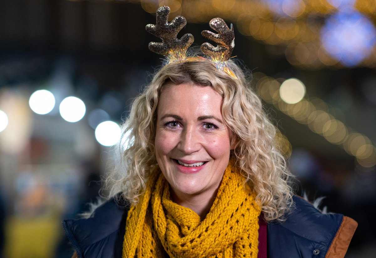 kobieta w wieku 40 plus z różkami renifera i z żółtym szalikiem uśmiecha się stojąc na ulicy