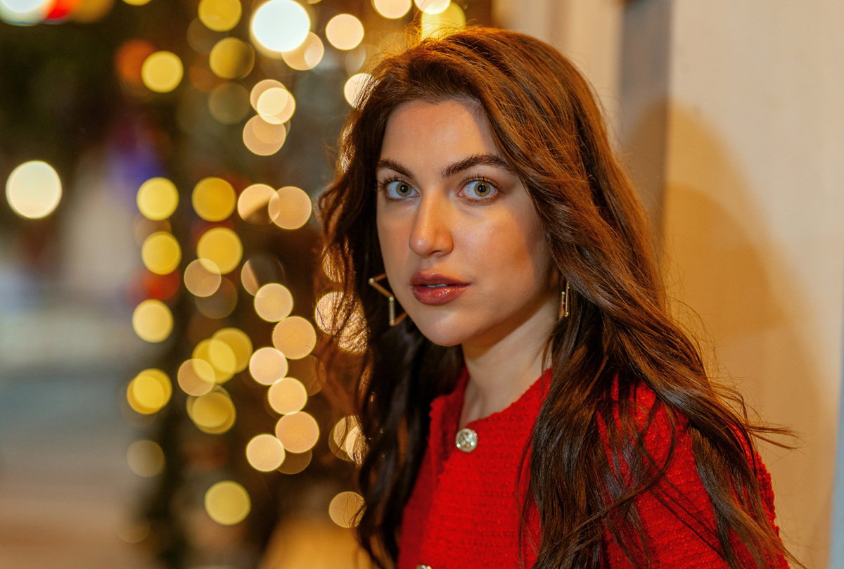 kobieta w wieku około 25 plus w czerwonym żakiecie z wystraszonym wyrazem twarzy na tle światełek