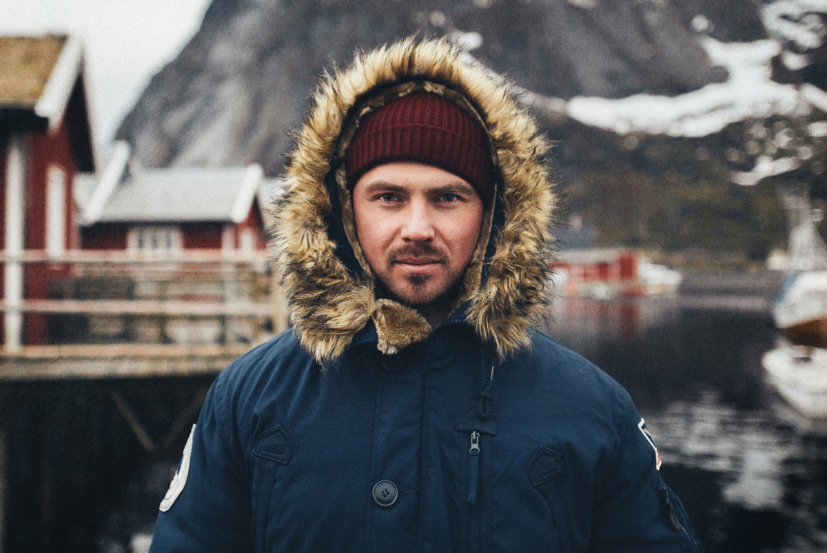 mężczyzna w wieku 35 plus w kurtce z kapturem stoi zamyślony na tle norweskiego pejzażu