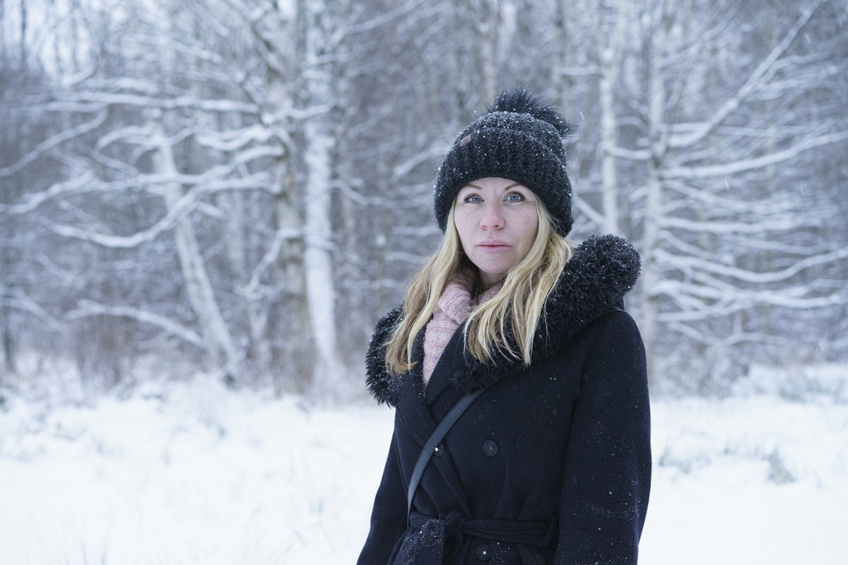 kobieta w wieku 35 plus w płaszczu i czapce na spacerze w zaśnieżonym plenerze stoi smutna