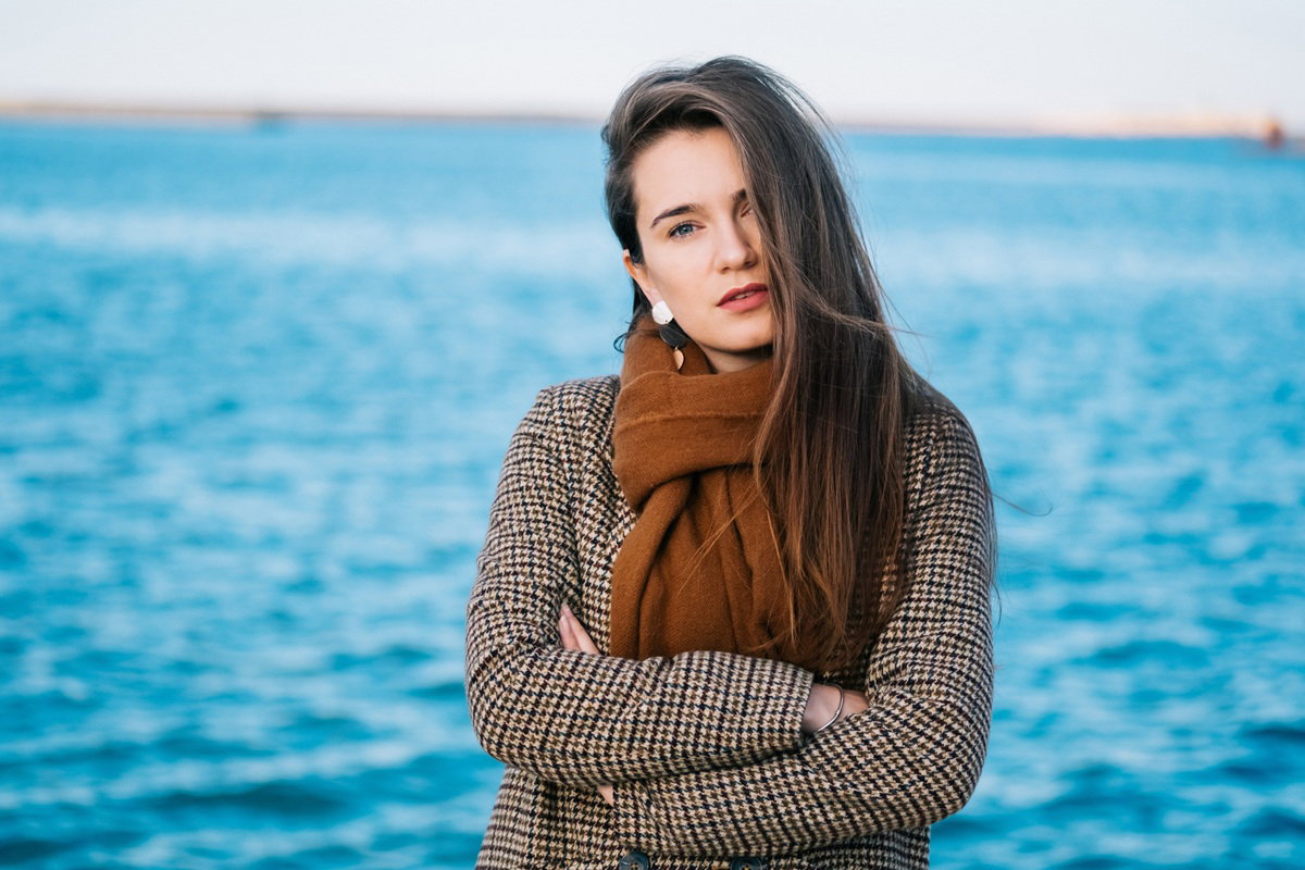 kobieta w wieku 30 plus w brązowym szalu z poważnym wyrazem twarzy na tle morza