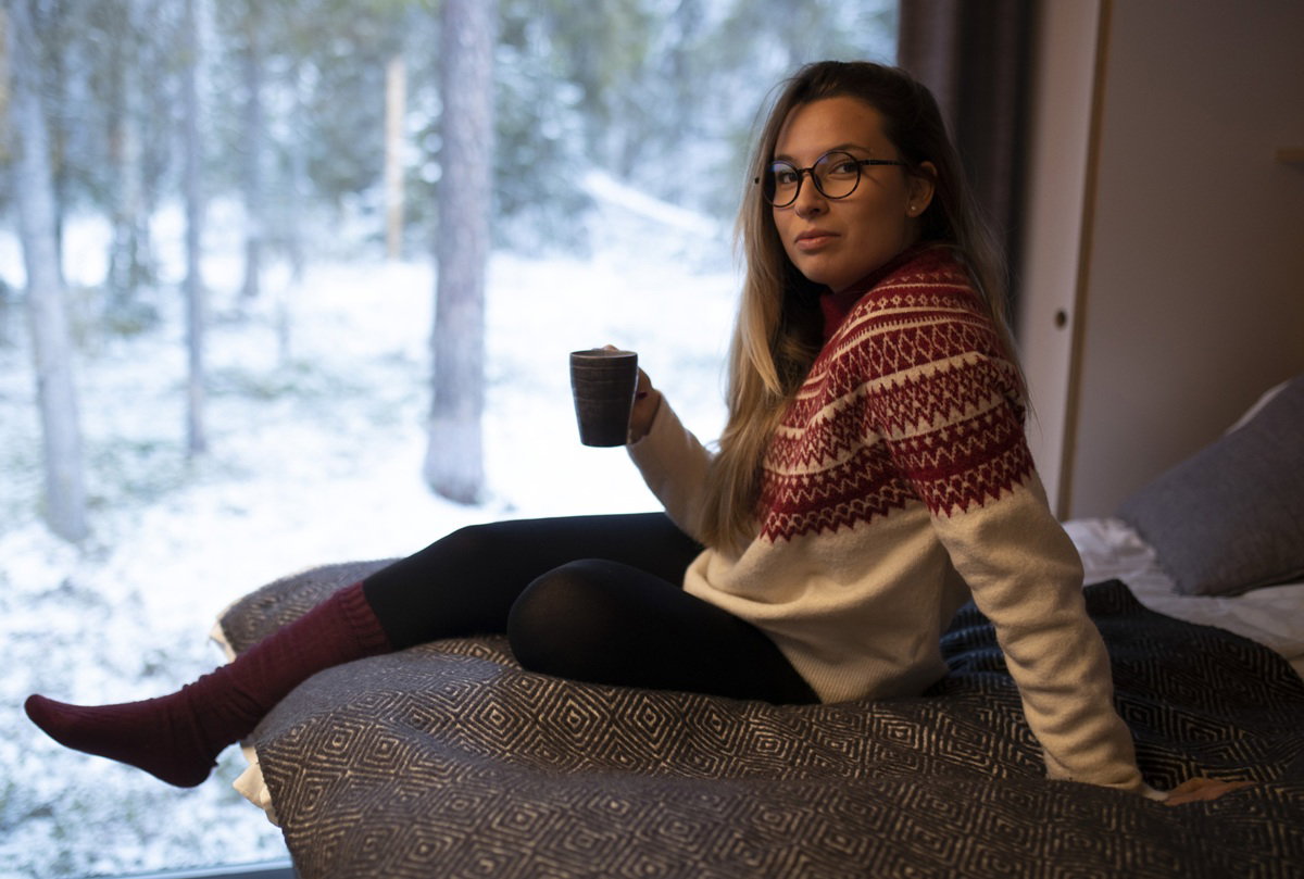kobieta w wieku 25 plus w okularach siedzi przy oknie przy zimowym pejzażu z kubkiem gorącego napoju