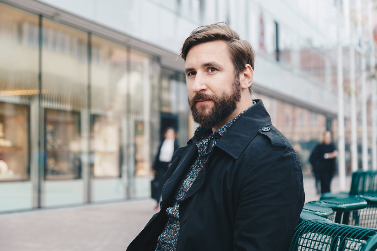 mężczyzna w wieku 40 plus z wąsami i brodą siedzi na ulicy zamyślony