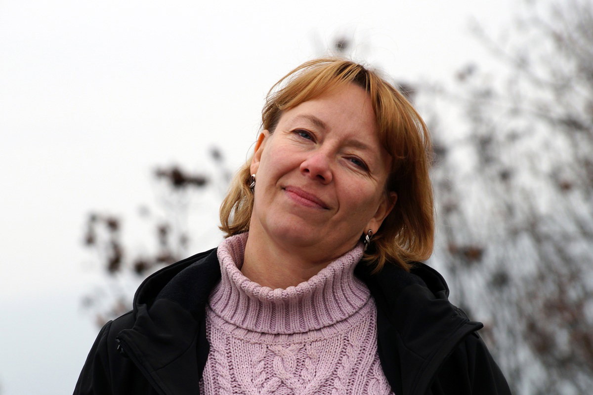 kobieta w wieku 50 plus w różowym swetrze stoi na zewnątrz i się uśmiecha