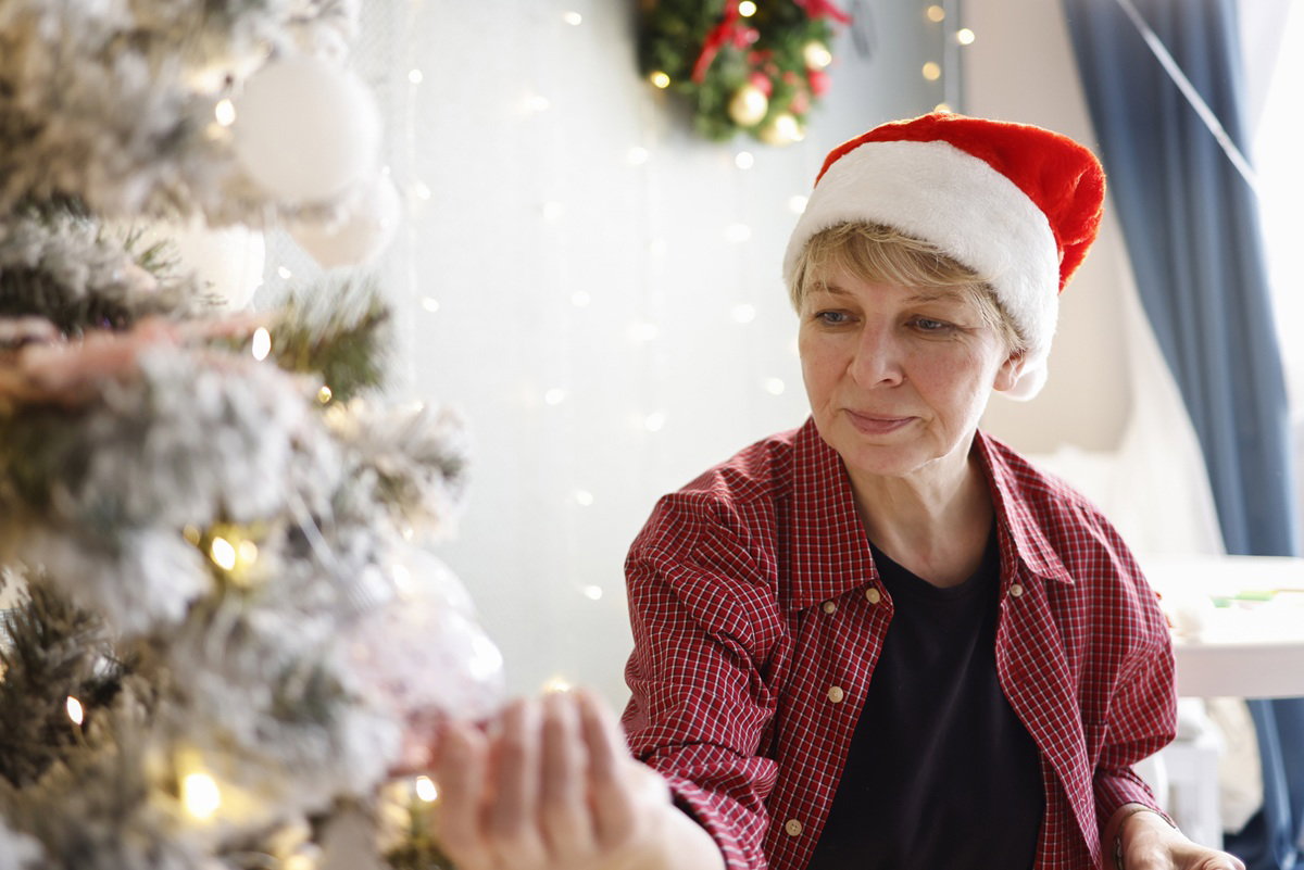 kobieta w wieku 50 plus siedzi przy choince w czapce Mikołaja zamyślona