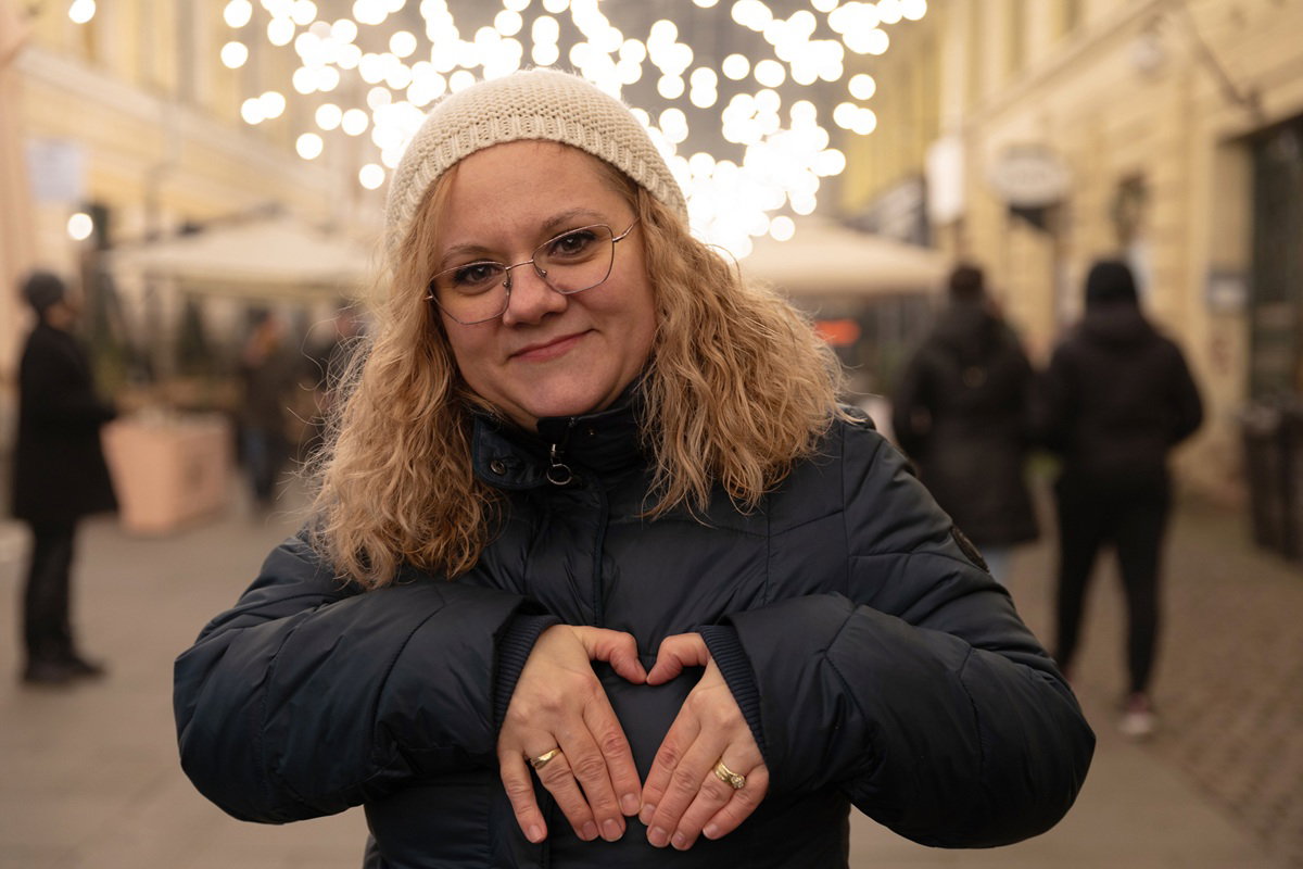 kobieta w wieku 40 plus w okularach stoi na ulicy i robi serduszko z dłoni