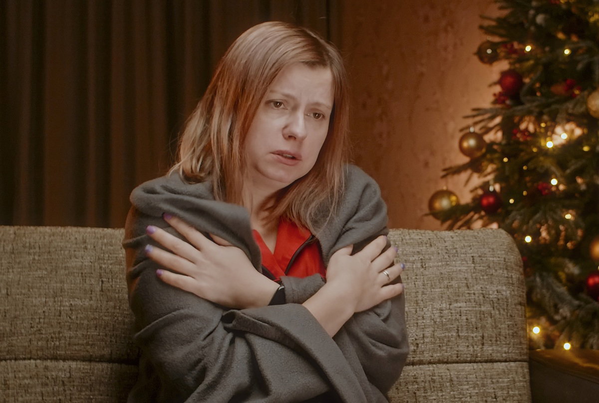 kobieta w wieku około 30 lat siedzi na kanapie w kocu przy choince zrozpaczona.