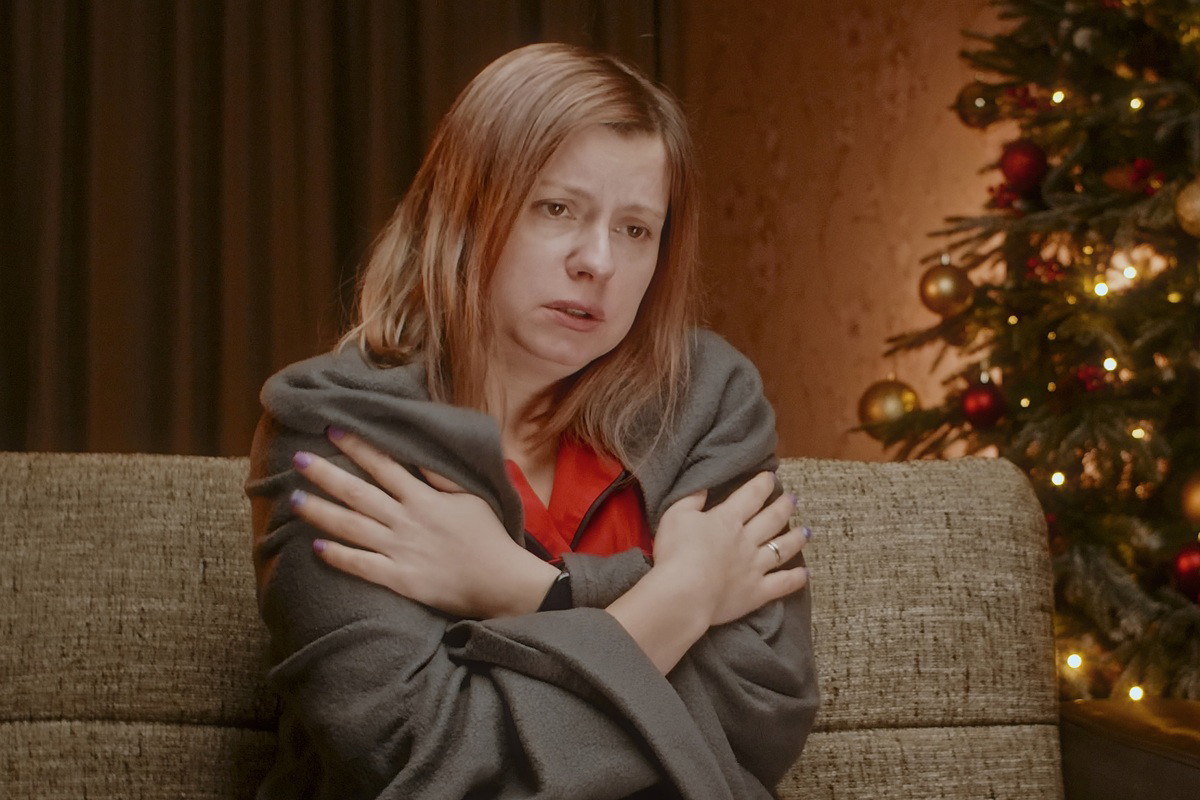 kobieta w wieku około 30 lat siedzi na kanapie w kocu przy choince zrozpaczona.