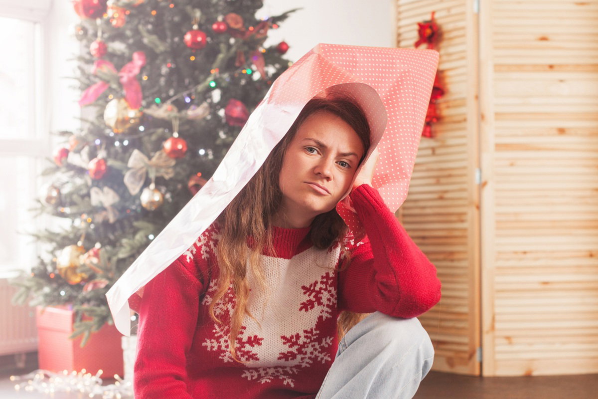 kobieta w wieku 35 plus siedzi w papierze na głowie na tle choinki z powątpiewającą miną