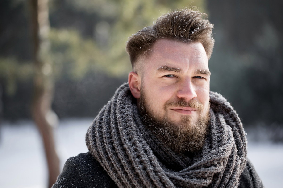 mężczyzna w wieku prawie 40 lat z grubym szalem na szyi stoi na zewnatrz poważny