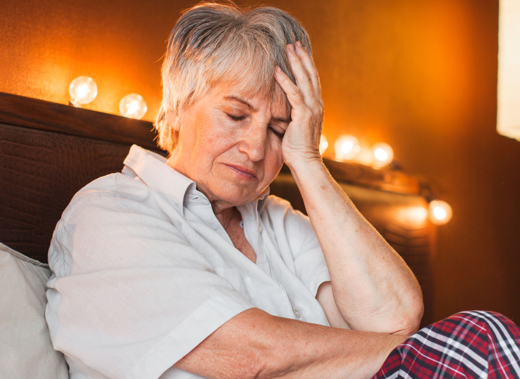 Sad unhappy senior woman seated on bed in bedroom
