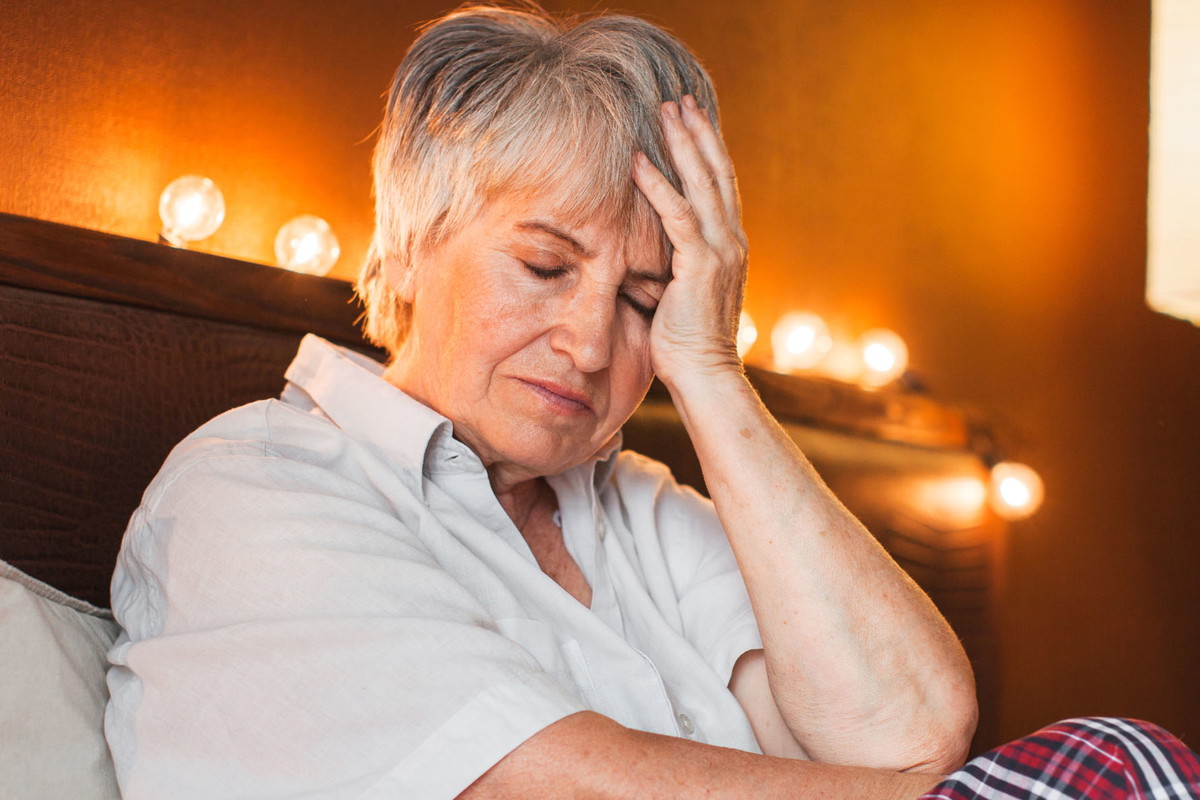Sad unhappy senior woman seated on bed in bedroom