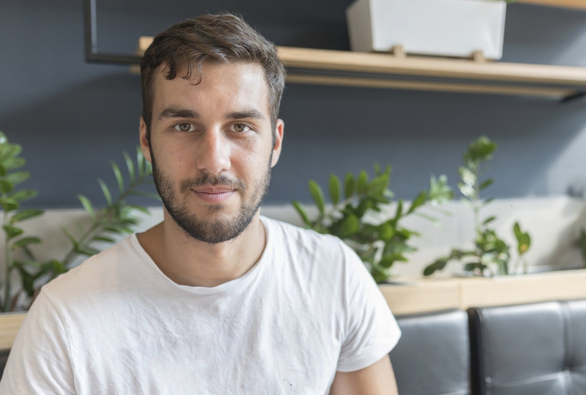 mężczyzna w wieku 25 plus w białym t-shircie siedzi na kanapie i lekko się uśmiecha