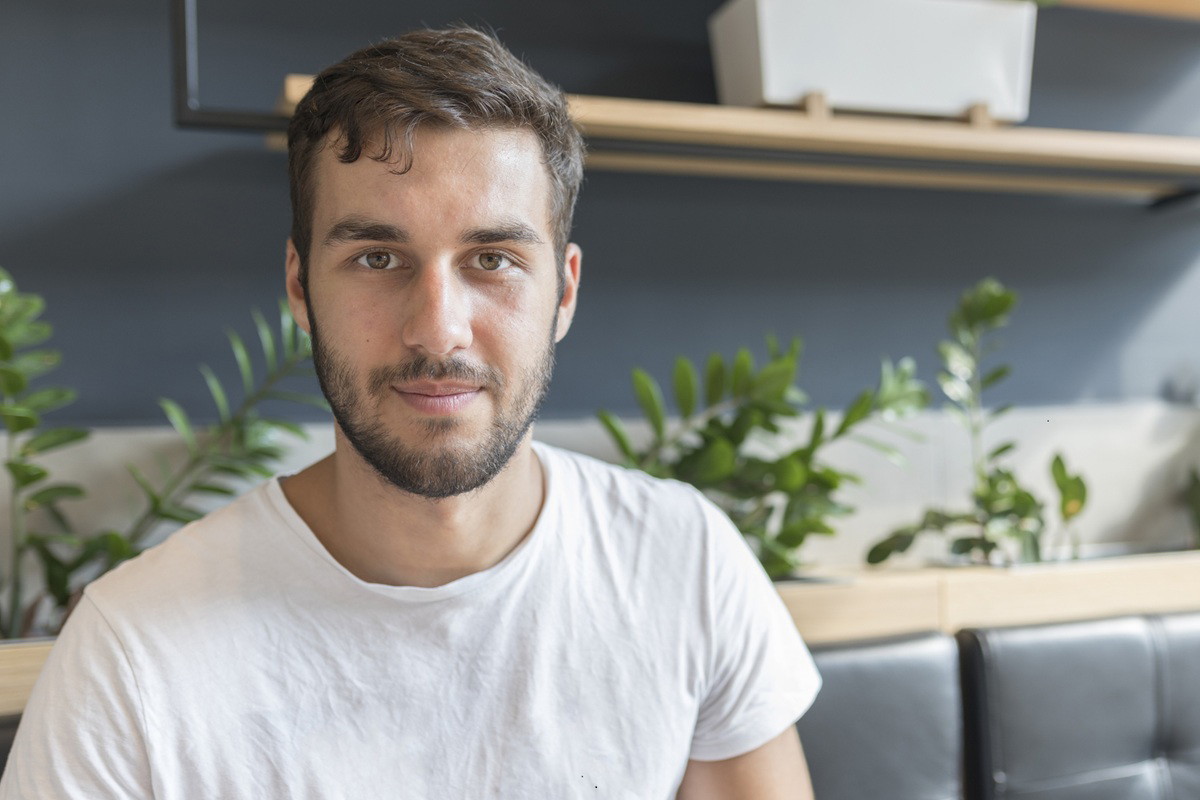 mężczyzna w wieku 25 plus w białym t-shircie siedzi na kanapie i lekko się uśmiecha