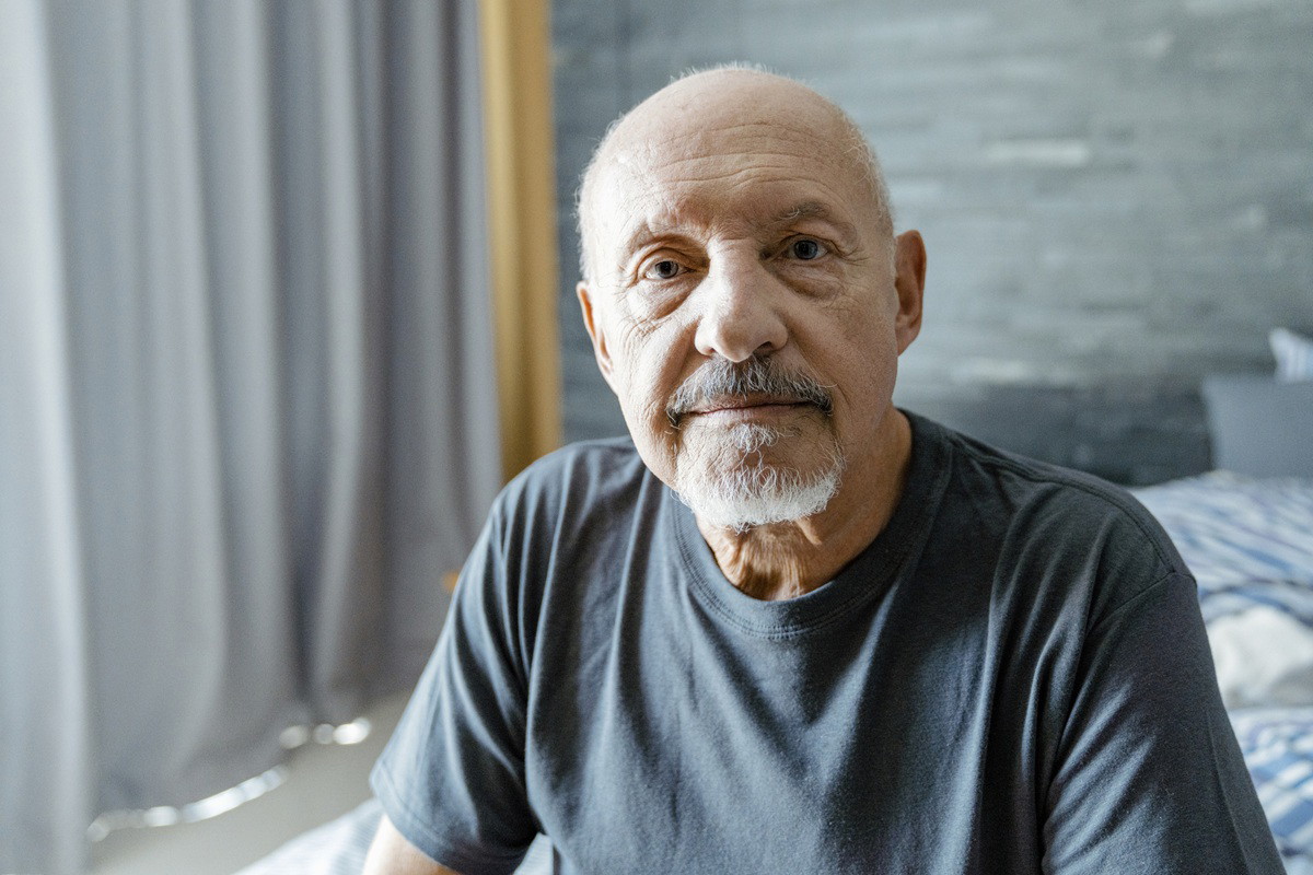 mężczyzna w wieku 71 lat siedzi na łóżku zmartwiony