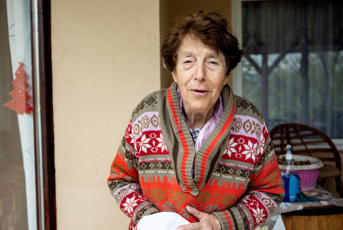 kobieta w wieku 70 plus we wzorzystym swetrze stoi przed domem zatroskana