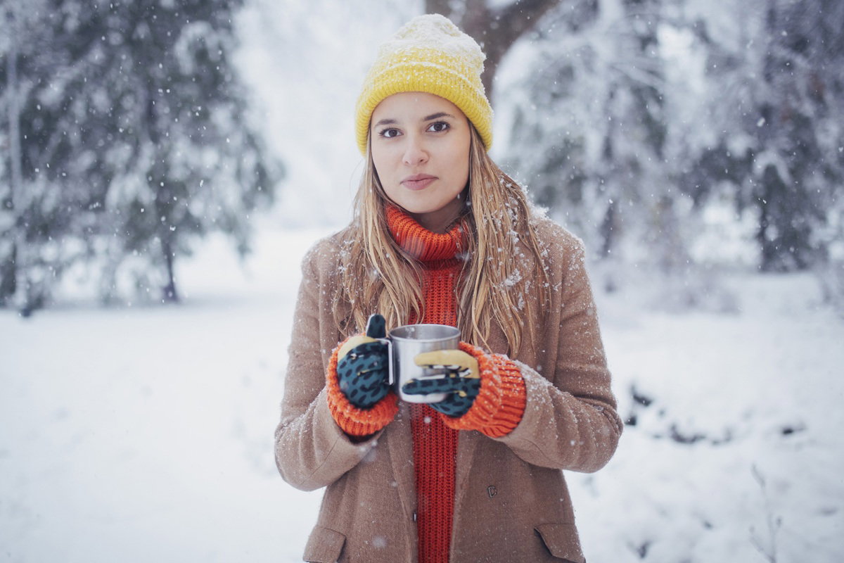 kobieta w wieku 25 plus stoi na tle zimowego pejzażu z kubkiem w ręce