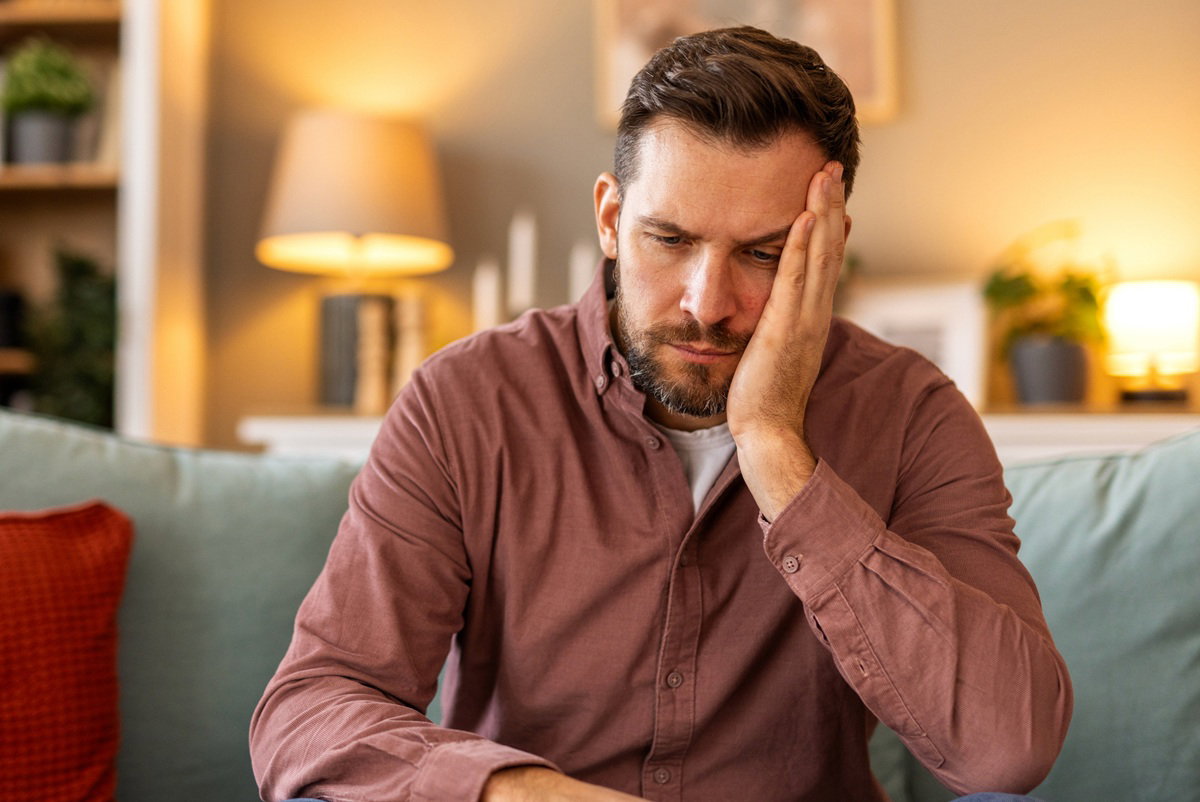 mężczyzna w wieku około 40 plus z brodą i wąsami w jasnej koszuli siedzi na kanapie zmartwiony