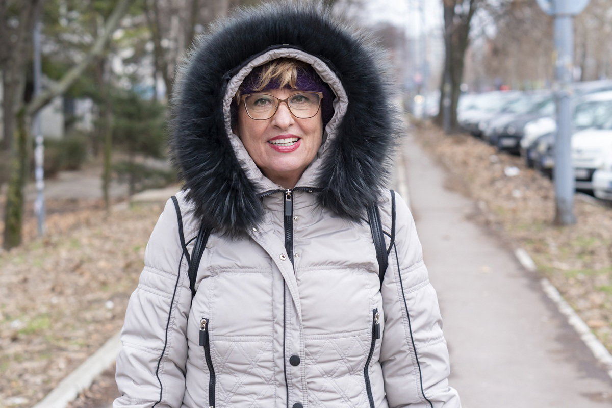 kobieta w wieku 60 plus w okularach stoi na ulicy w kapturze zadowolona