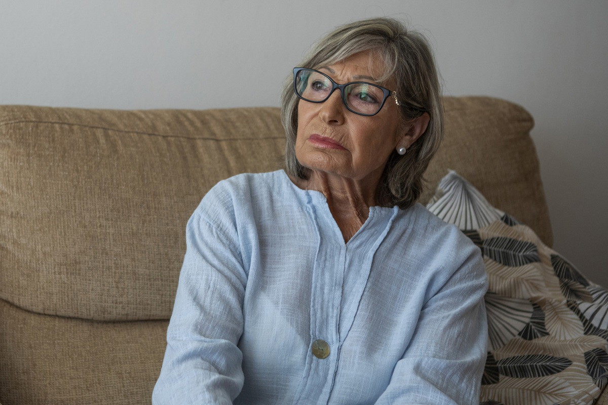 elegancka kobieta w wieku 70 plus w okularach siedzi na kanapie zamyślona i smutna