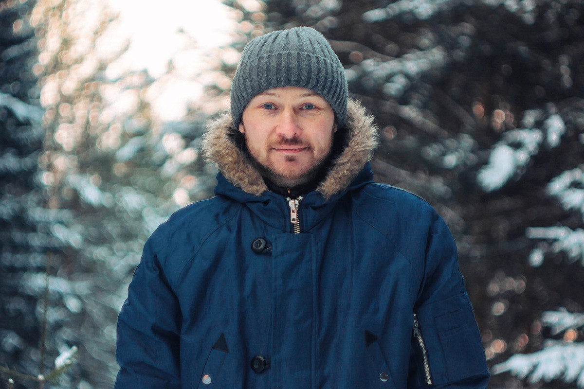 mężczyzna w wieku 35 plus stoi na zewnątrz na tle zaśnieżonych drzew i lekko się uśmiecha